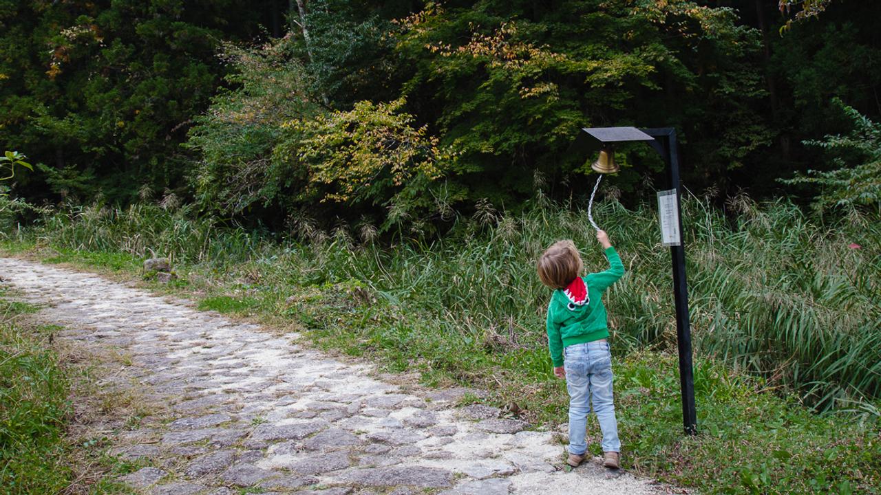 Small boy ringing bell on the side of a path Japan Ancient Trails